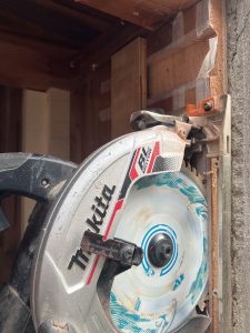 傾いている既存窓枠を垂直にするために丸ノコを窓枠横へ当ててカットする