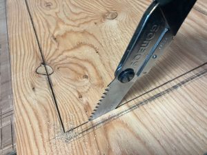 モルタル壁用の構造用合板をサッシ部分を開口するため墨にあわせて手ノコを引く
