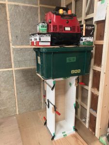 ダボを木工用ボンドで取り付け組み立てた埋め込み型造り付け収納ウォールキャビネットを側面はクランプで、上からはエアーコンプレッサーや材料等重いもので押さえてボンドが乾燥するまで待つ